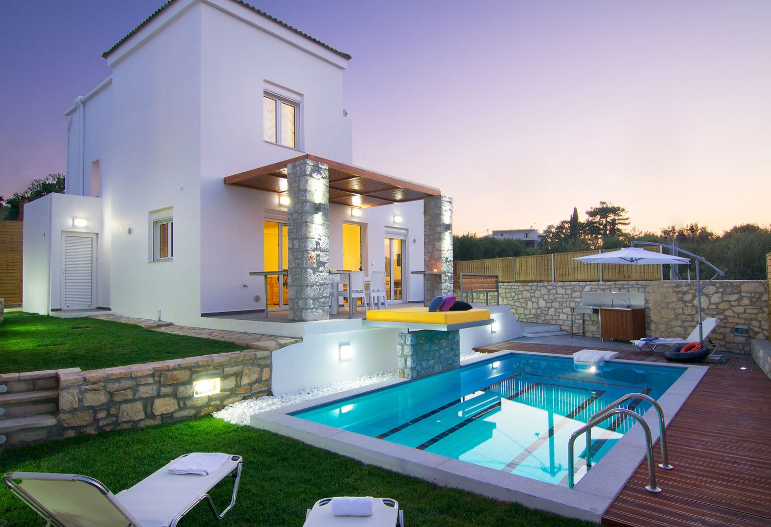 Villa Aada in the evening: lit house with a turquoise glowing pool and lawn