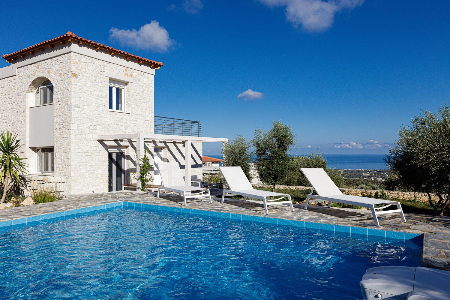 Villa Eos: stone house with a long pool, sun loungers and a view over olive groves to the sea